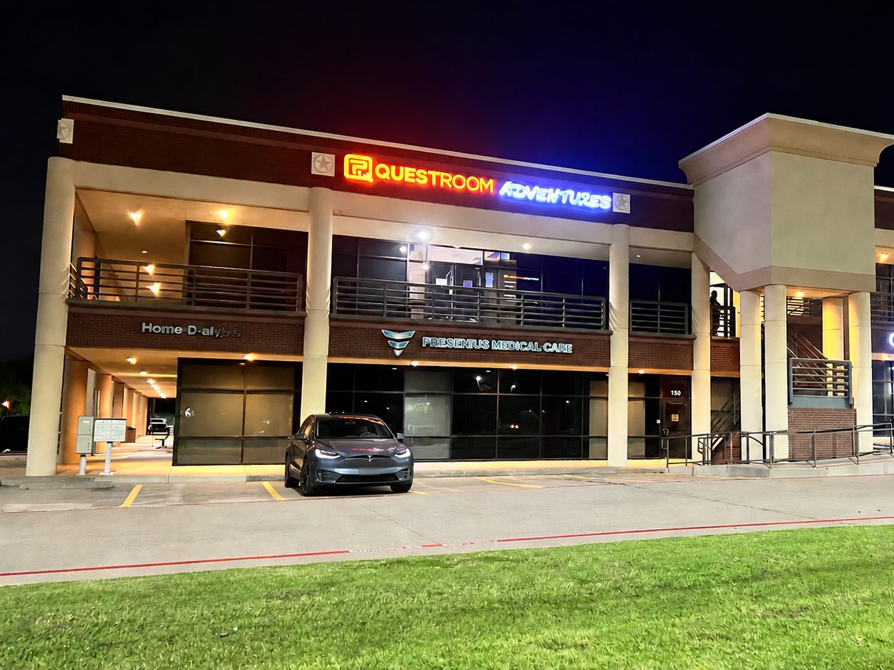 Quest Room Adventures escape rooms in Plano, Texas, with the lit sign at 3420 K Ave at night