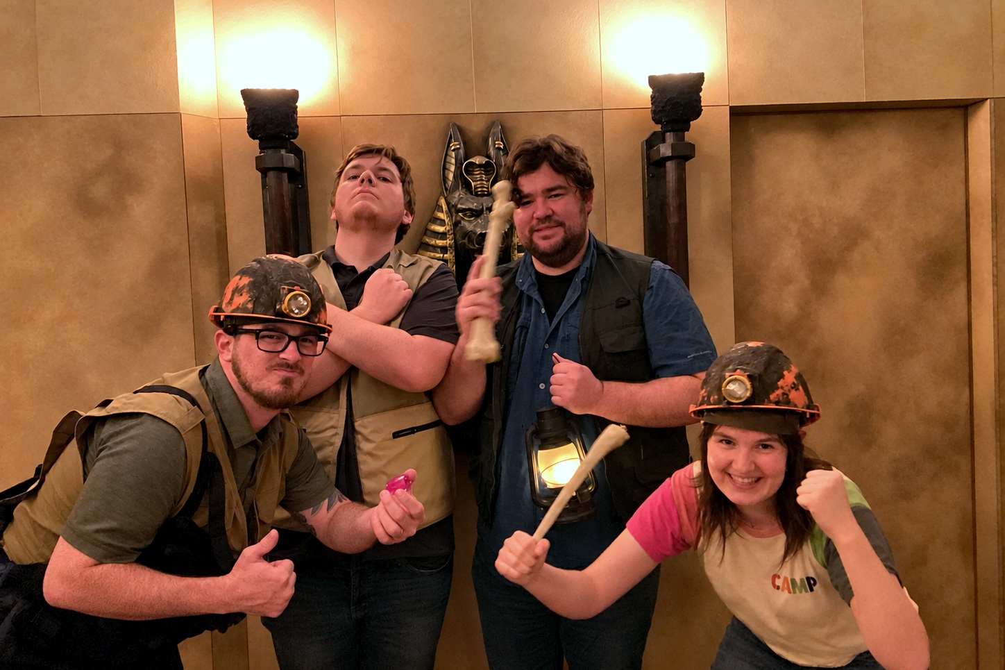 Four friends at an escape room bachelor party pose in explorer gear with a lantern and bones inside Red Giant