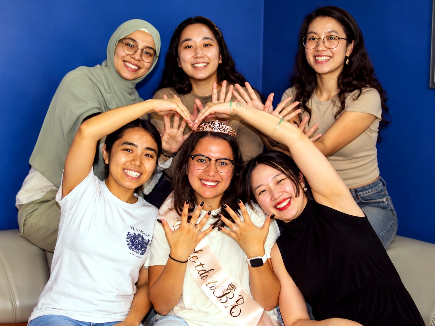 Bachelorette group at an escape room party frames the bride with heart-shaped hands in the Quest Room lobby